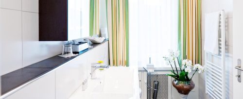 Modernes Badezimmer im Hotel Amaris mit Waschbecken, großem Spiegel und Fenster mit Tageslicht.