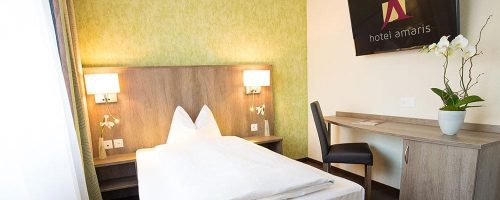 Helles Einzelzimmer im Hotel Amaris mit Bett, Arbeitsplatz und grüner Akzentwand.