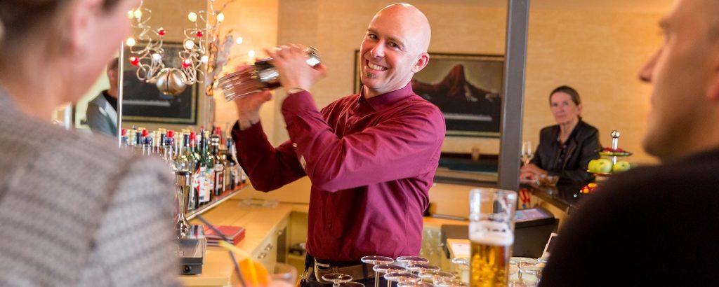 Barkeeper bereitet frischen Cocktail an der stilvollen Hotelbar für einen Gast zu.
