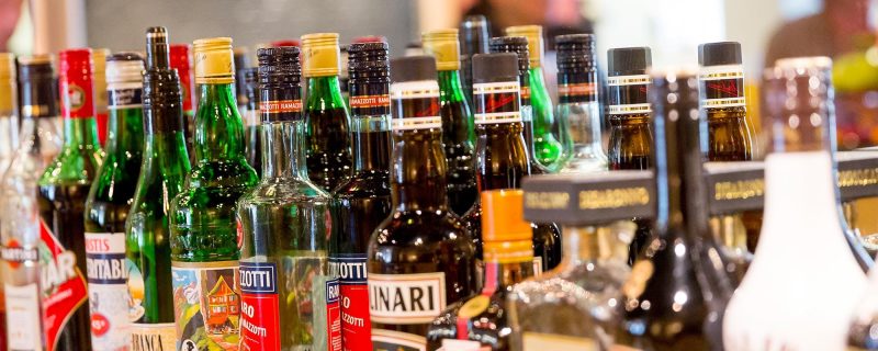 Selection of spirits and liqueurs at the hotel bar, blurred guests chatting in the background.