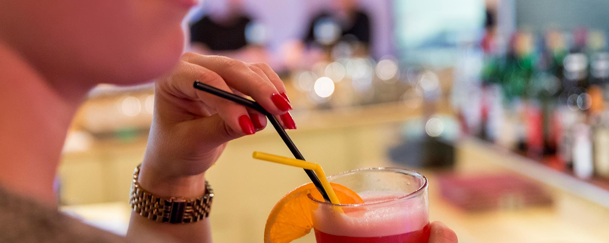 Guest with red drink and straw at the bar, modern art in the background.