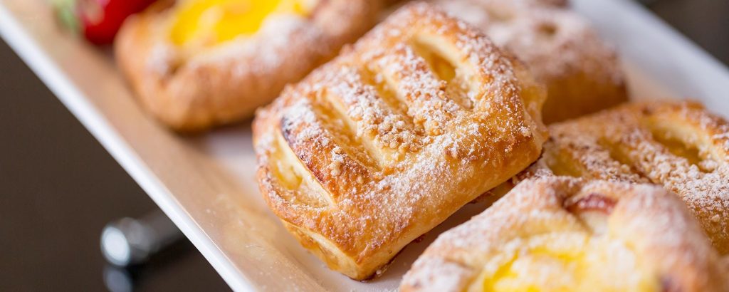Süße Plunderteilchen mit Vanillefüllung und Puderzucker am Frühstücksbuffet.