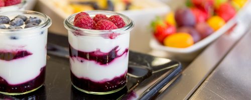 Joghurt mit Beeren und Fruchtsauce im Glas am Frühstücksbuffet.