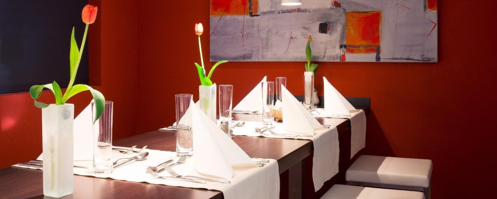 Stilvoll gedeckter Restauranttisch mit Gläsern, gefalteten Servietten und Blumenvasen in modernem Ambiente.