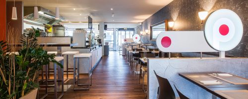 Moderner Restaurantbereich im Hotel Amaris mit offenen Sitzplätzen, Bar, Küche und stilvoller Beleuchtung.