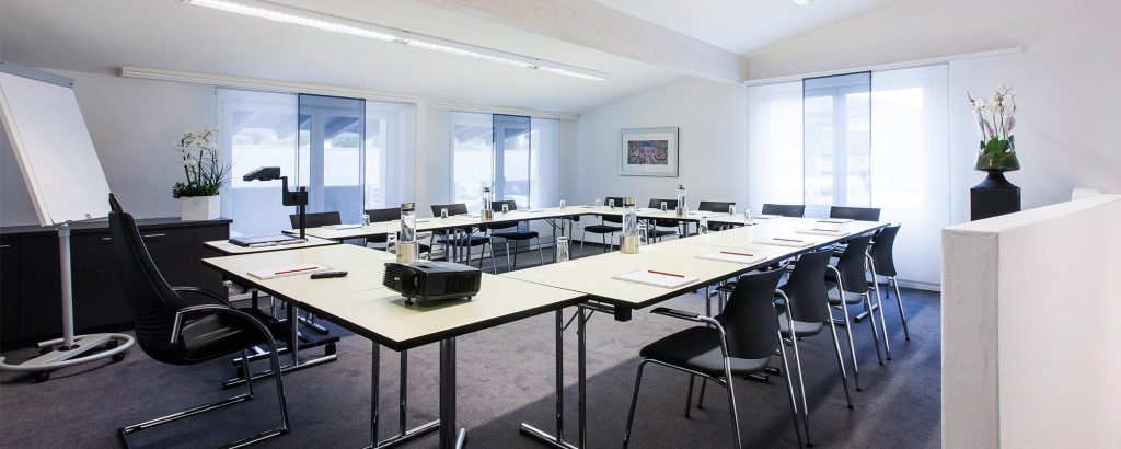 Moderner Seminarraum im Hotel Amaris mit U-förmig angeordneten Tischen, Stühlen, Beamer und Tageslicht durch große Fenster.