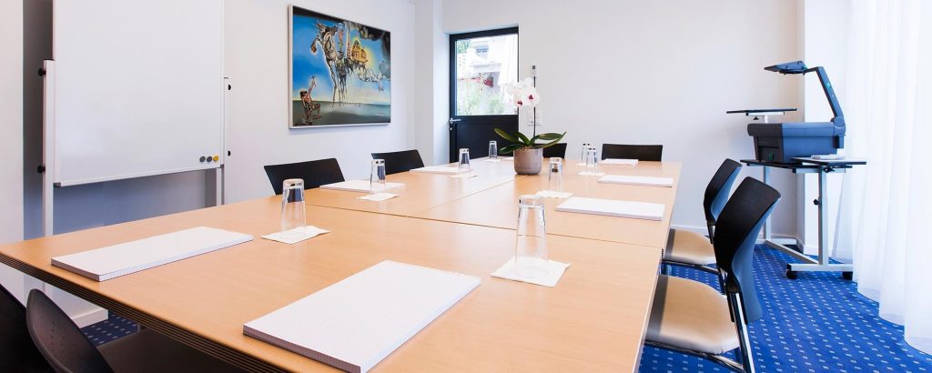 Heller Seminarraum im Hotel Amaris mit Konferenztisch, Stühlen, Flipchart und Präsentationstechnik.