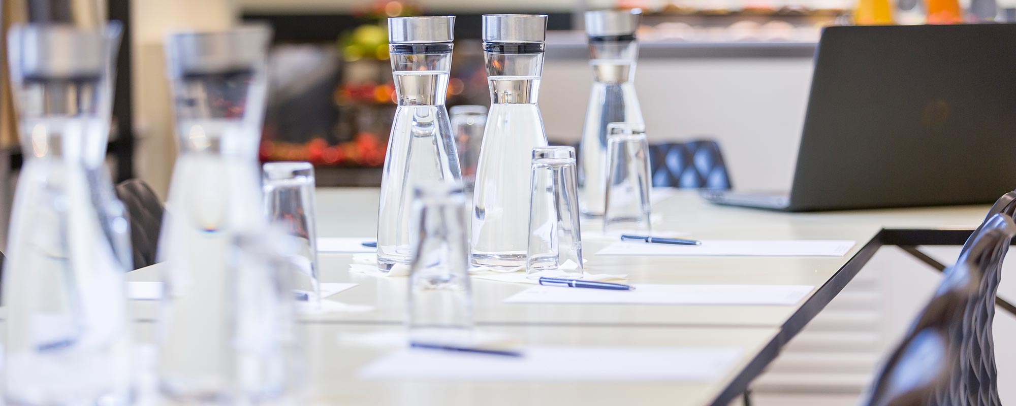 Close-up of a conference table with water carafes, glasses, notepads and a laptop for a meeting.