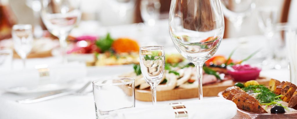 Gedeckter Tisch mit Gläsern und verschiedenen Speisen wie Vorspeisen, Gemüse und Fleisch in stilvollem Ambiente.