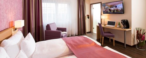 Helles Businesszimmer im Hotel Amaris mit komfortablem Bett, Schreibtisch und Tageslicht.