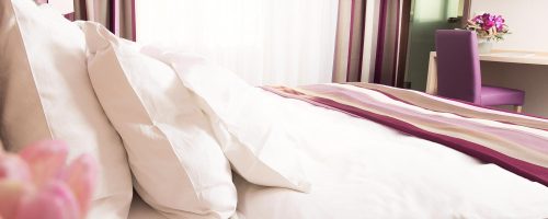 Detailaufnahme des Bettes im Businesszimmer des Hotel Amaris mit weißen Kissen und gestreifter Tagesdecke.