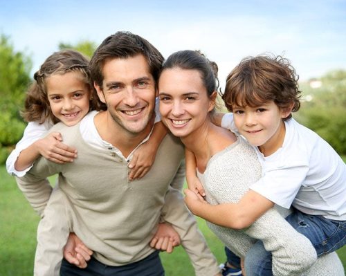 Glückliche Familie mit zwei Kindern im Freien, die sich umarmen und gemeinsam in die Kamera lächeln.