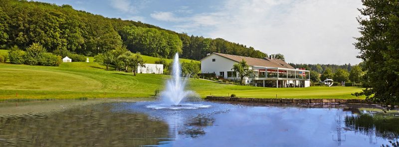 Golfanlage mit Teich und Springbrunnen, Clubhaus und gepflegter Landschaft in ruhiger Umgebung.