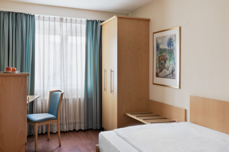 Helles Einzelzimmer im Hotel Amaris mit Bett, Arbeitsplatz und Kleiderschrank.